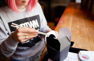 girl with pink hair eating chinese food. hands holding chopsticks
