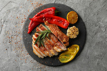 Tray with chopped pork steak and vegetables on gray background. Grilled food