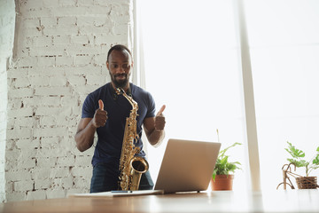 African-american musician playing saxophone during online concert at home isolated and quarantined....