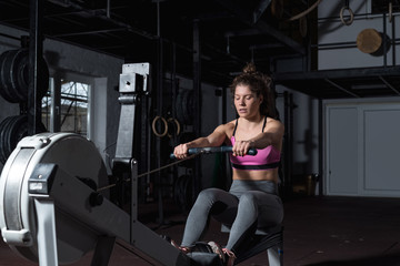 Young strong fit sweaty powerful attractive muscular woman with big muscles doing hard core row heavy cross training workout on indoor rower at the gym real people rowing exercise © Srdjan