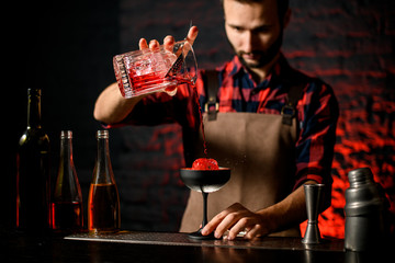 bartender accurate pours red campari drink from mixing cup to wineglass