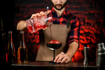 bartender professionally pours red campari drink from mixing cup to wineglass