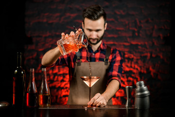 male bartender pours cocktail from mixing cup into metal martini glass.