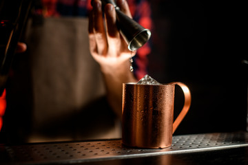 close-up metal cup over which bartender's hand hold jigger