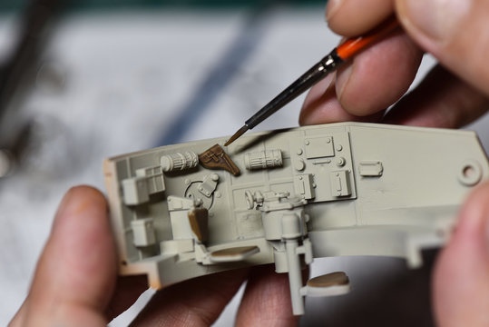 Plastic Modeling and model building. Close up of male hands painting and assembling scale model of a tank. Hobby and leisure at home. Hobbies in quarantine. Modelism macro shot. 