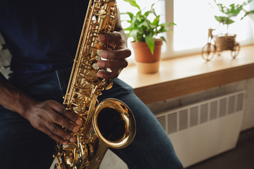 Obraz premium African-american musician playing saxophone during online concert at home isolated and quarantined. Using camera, laptop, streaming, recording courses. Concept of art, support, music, hobby, education