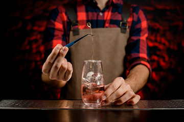 male bartender decorates by plant glass with cold alcoholic cocktails
