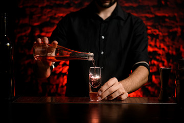 bartender in black shirt pours drink from bottle into small glass