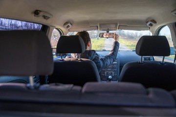 young driver adjusts the rearview mirror in a car