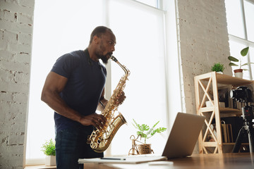 African-american musician playing saxophone during online concert at home isolated and quarantined....