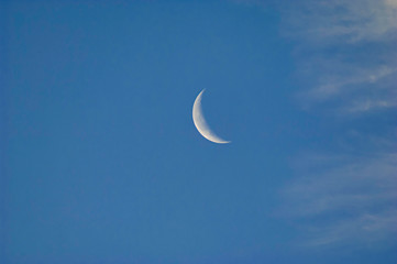 Obraz na płótnie Canvas A slim sliver of the silvery moon set on an expanse of a partly cloudy blue sky.