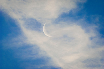Naklejka na ściany i meble A slim sliver of the silvery moon set on an expanse of a partly cloudy blue sky.