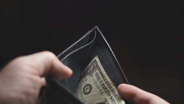 close-up of a man's hands on a dark background, one dollar in his wallet. Budget and expenses.