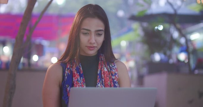 4K Young Asian woman staring at laptop screen, working outdoors in the city at night