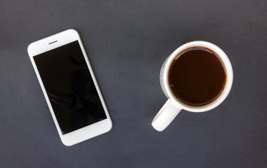 Fototapeta na wymiar Black table with a white smartphone and a white mug with black coffee.
