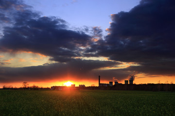 Kolorowy zachód słońca nad obszarem wiejskim, złote i burzowe chmury, zielony rzepak.