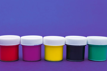 Large set of acrylic paint cans in a row. Colorful paints neon blue and violet background with copyspace.