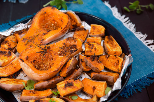 Close up baked roasted grilled whole orange pumpkin butternut squash and sweet potato slides with herbs on the baking sheet on blue napkin. Vegetarian and vegan food diet. Healthy eating concept.