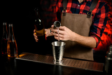 Close-up man bartender pours cocktail from bowl into metal martini glass.