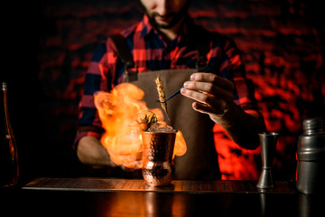 professional bartender decorates with spikelet metal glass and make fire near it.