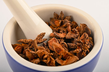star anise in a blue ceramic spice mortar with a pestle on a white background. Close up.