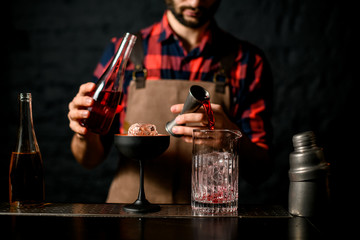 Man bartender pours red liquid from jigger into mixing cup