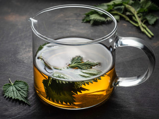 Fresh nettle tea in glass pot on wooden vintage table.