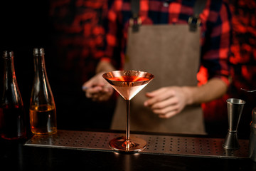 Close-up of metallic martini glass with cocktail stands at bar counter.