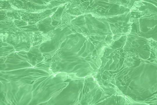 Closeup of calm clear water surface with water splashes in trendy mint color. Swimming pool water texture. Trendy fresh abstract nature background. 2020 color trend concept.