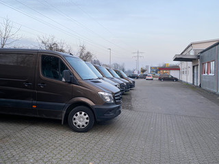 Side view of row brown transportation delivery vans being parked in front of warehouse building with dramatic sky modern logistics for ecommerce sector