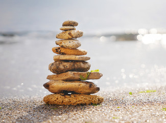 Fototapeta na wymiar Stones pyramid on sand symbolizing zen, harmony, balance. Ocean in the background. Soft focus.