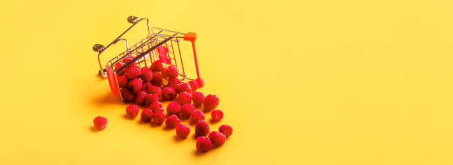 Turned shopping cart with ripe raspberries on orange background © alesmunt