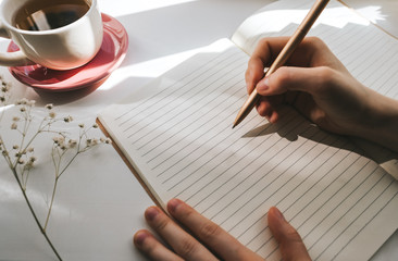 Woman takes notes in a notebook on a sunny morning near the window.