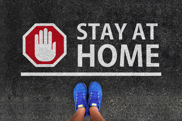 stay at home. man with a shoes is standing next to line and word stay at home and hand stop sign on road asphalt. coronavirus self isolation concept