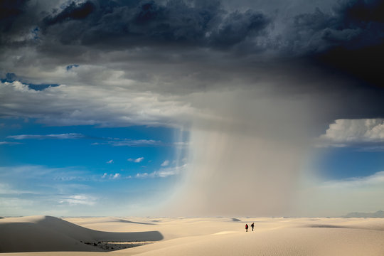 Rain falls across the desert as people hike