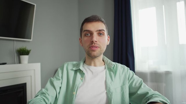 POV tilt up shot of young man setting camera and showing his drawings and notes in notepad during video call sitting at desk at home