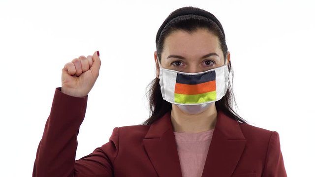 Virus and disease prevention concept. Woman wears a protective medical mask with the image of the flag of Germany. Shows the solidarity with the closed fist hand gesture. Demonstrate solidarity sign.