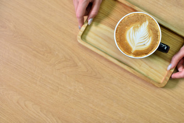 Female barista hands and a large cup of coffee with a pattern on the surface.