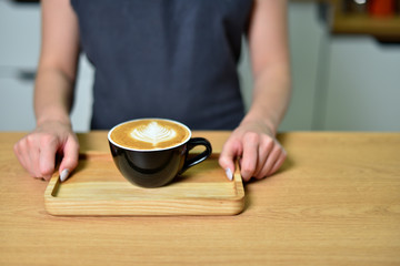 Female barista hands and a large cup of coffee with a pattern on the surface.