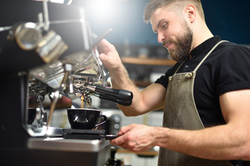 A young barista guy makes coffee on a large professional coffee machine. Small business and work concept for young people