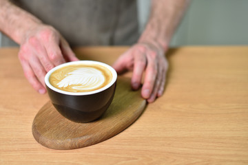 Male barista hands and a large cup of coffee with a pattern on the surface.