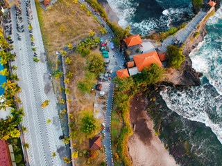 Tropical blue ocean with waves, temple on the coast, green palms and road. Top view aerial drone exotic landscape, Bali, Indonesia.