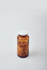 Vertical shot of a small brown glass bottle with white plastic lid, full of round yellow tablets, on white acrylic table