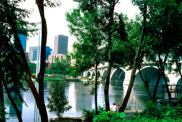 Downtown skyline across the Mississippi River flowing under the Stone Arch Bridge. Minneapolis Minnesota MN USA