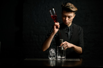 female bartender masterfully pours alcoholic drink into metal jigger.