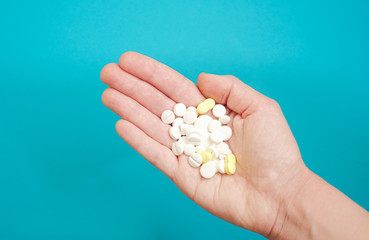 Hand holding pills on a turquoise background.