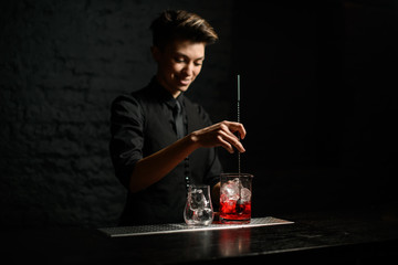 young woman bartender holds long metal spoon and mix cocktail