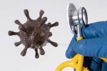 The concept of the detection of coronavirus. A doctor's hand holding a yellow stethoscope against a background of brown coronavirus.