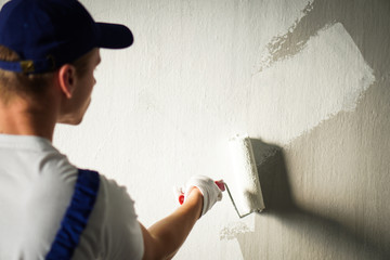Detail of a painter who is painting walls in a room on white colour.
