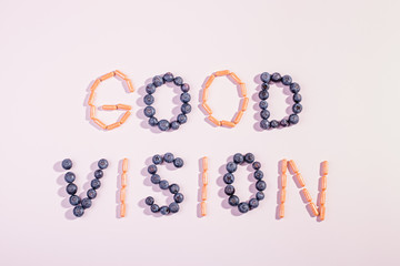 Vitamins and supplements for healthy eyes on pink background. How to maintain good vision concept. Blueberry and orange capsules forming words good vision, flat lay, top view